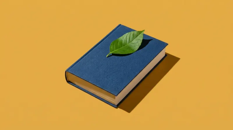 Libro de tapa azul oscuro con una hoja verde encima, fondo mostaza